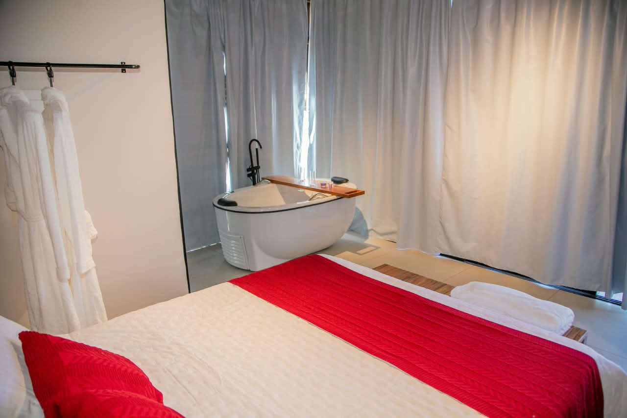 Quarto com cama de casal, roupões e banheira de imersão junto às cortinas claras