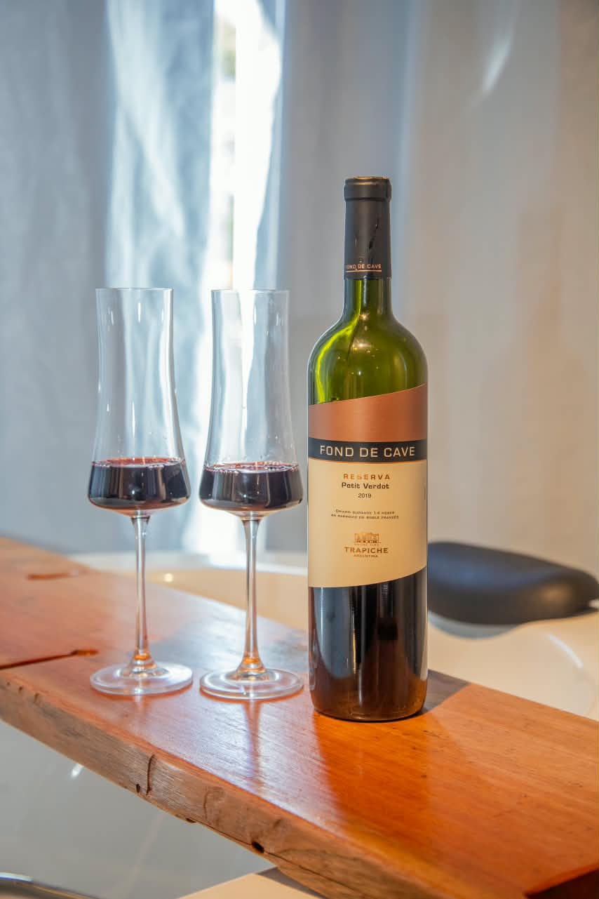 Garrafa de vinho e duas taças servidas sobre bancada de madeira, à luz da janela