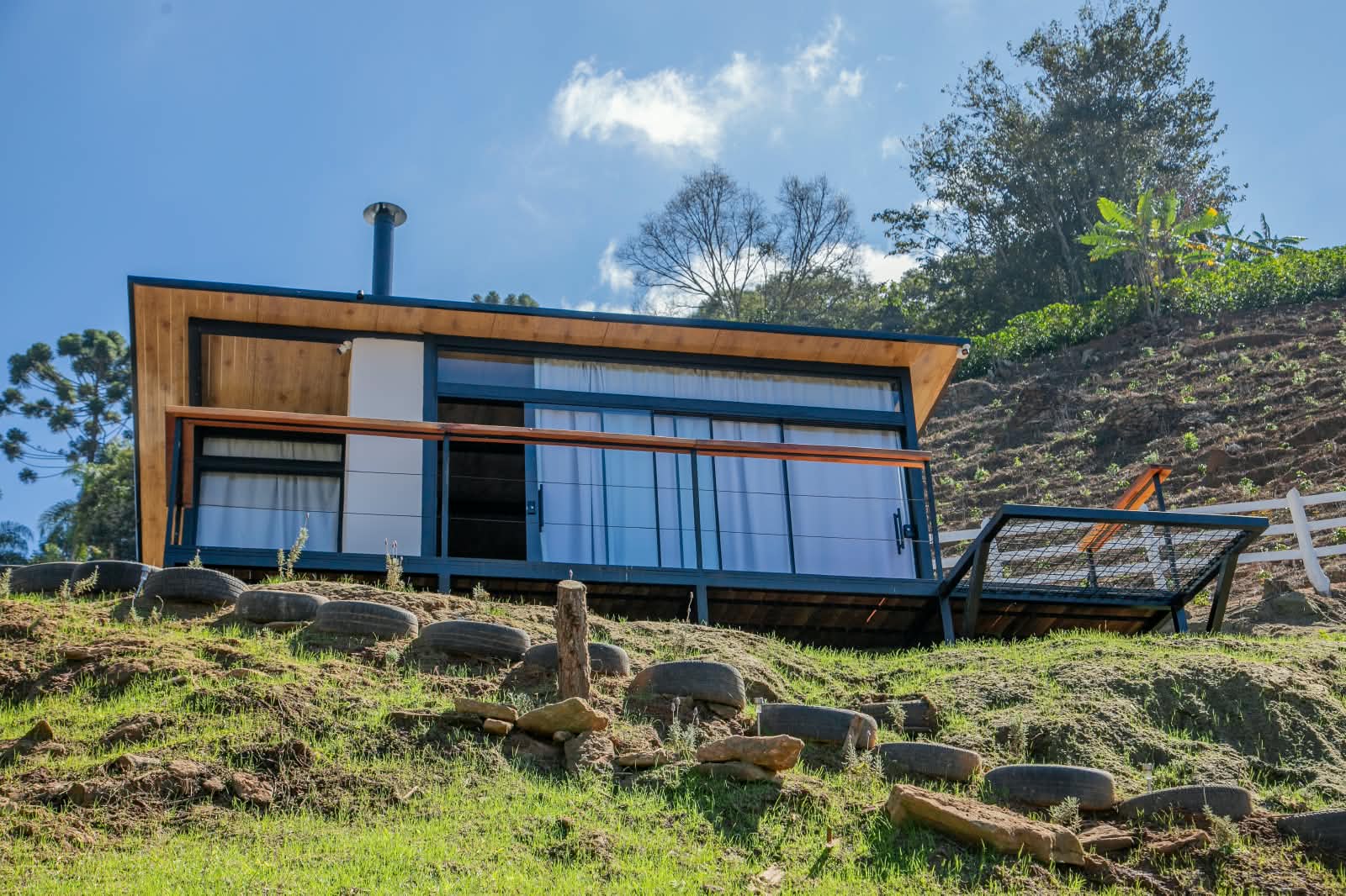Fachada da casa do Recanto do Anil em madeira e vidro, encaixada na encosta da serra de Cristina