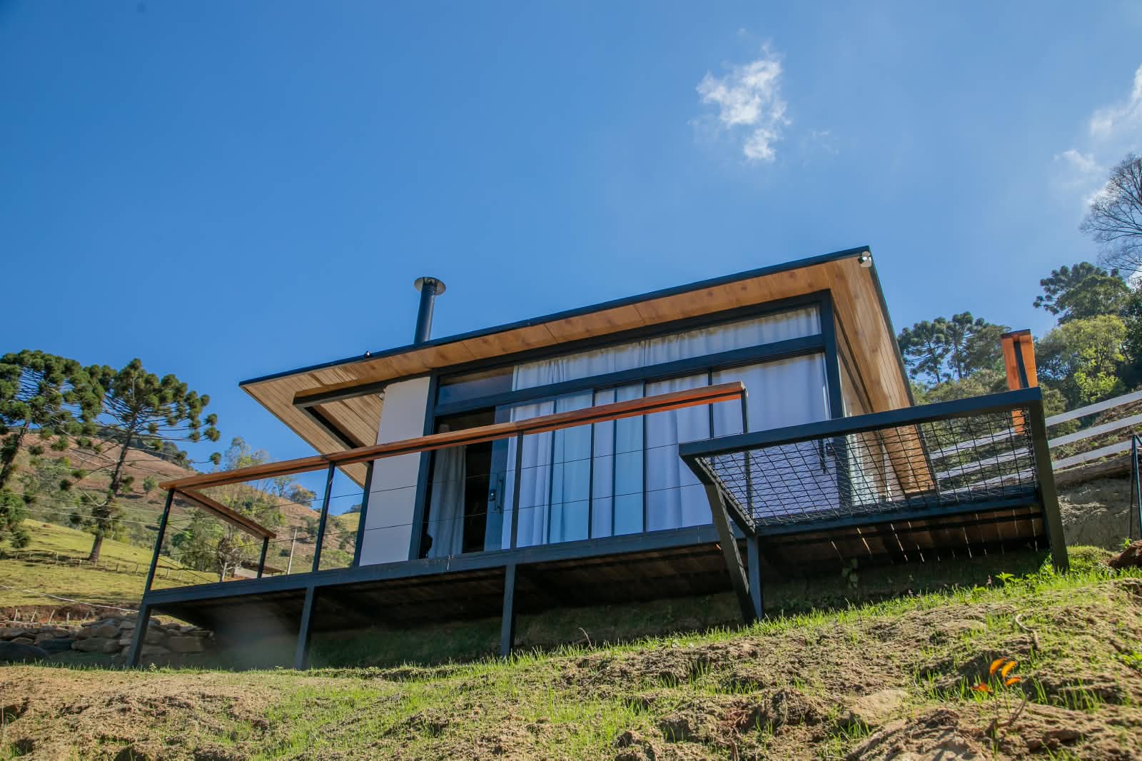 A casa vista de baixo, com varanda em madeira e araucárias ao redor